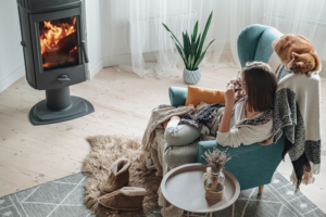 young woman cozy armchair plaid sitting by fireplace with domestic cat drinking tea home