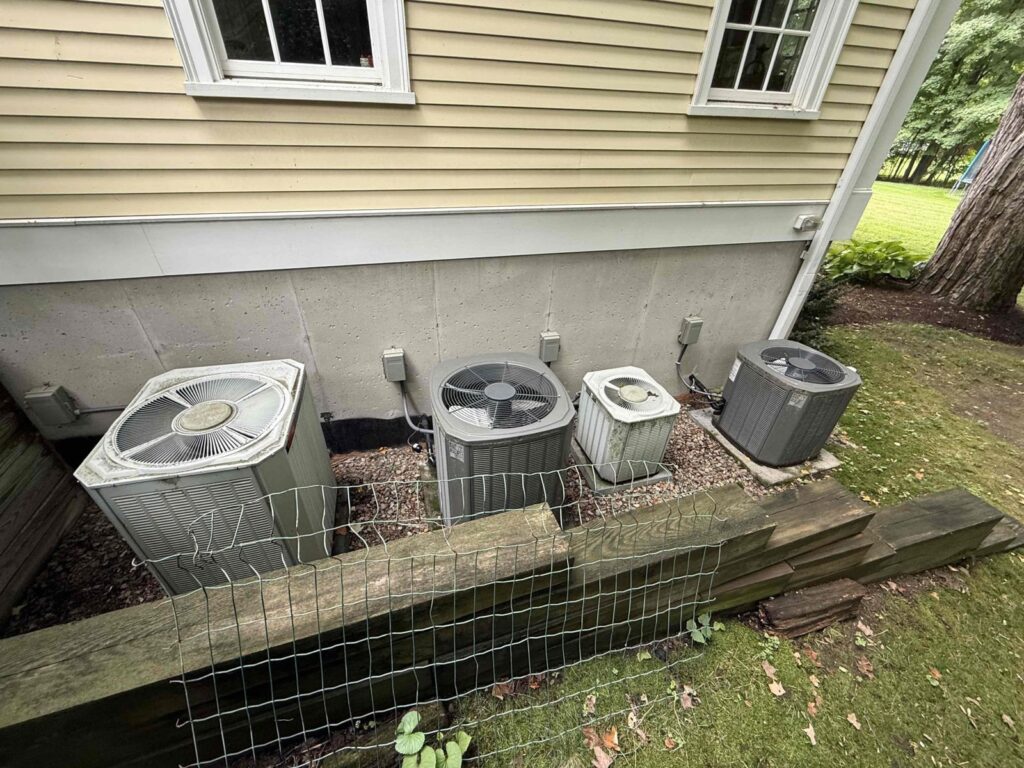 HVAC & Plumbing in Dover, MA 11 Four aging AC condensers from 2002 beside a Dover, MA home before replacement